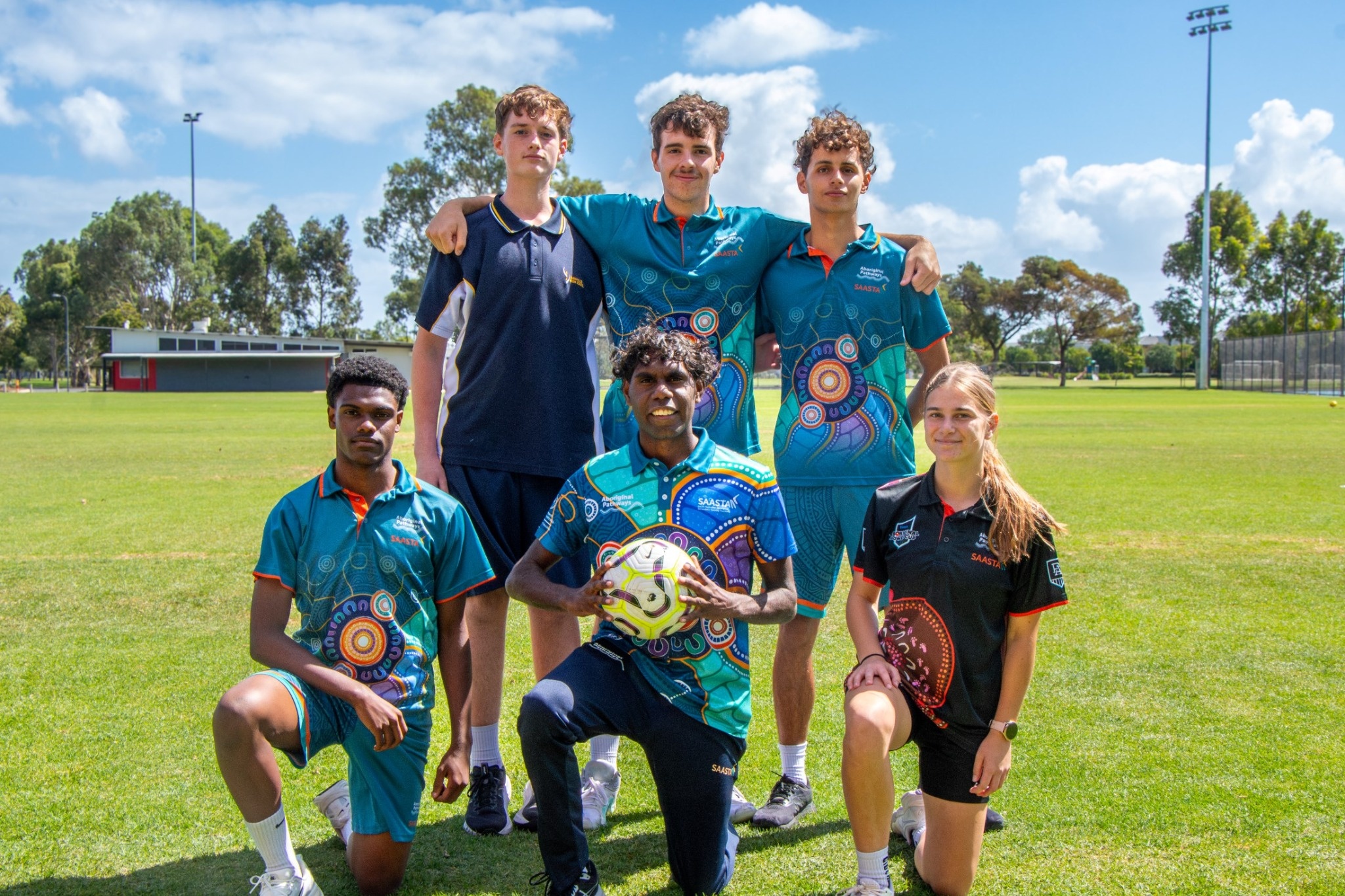 SAASTA students and coach posing with a soccer ball on a sports field.