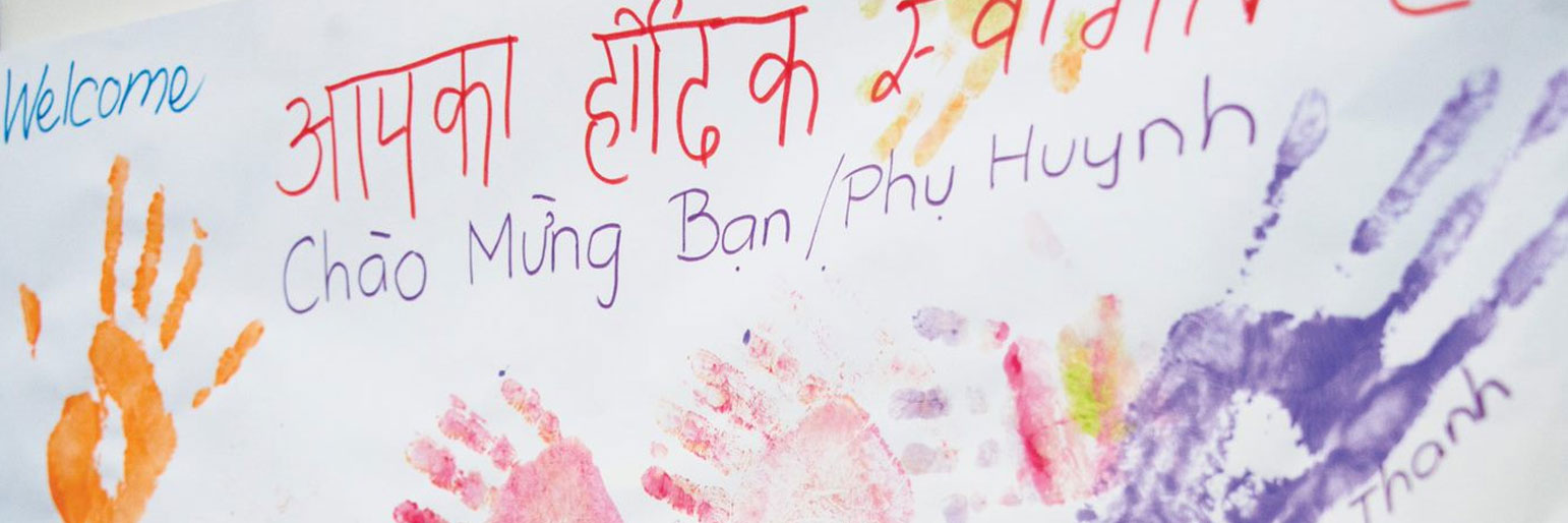 A sign with painted handprints and welcome messages in various languages