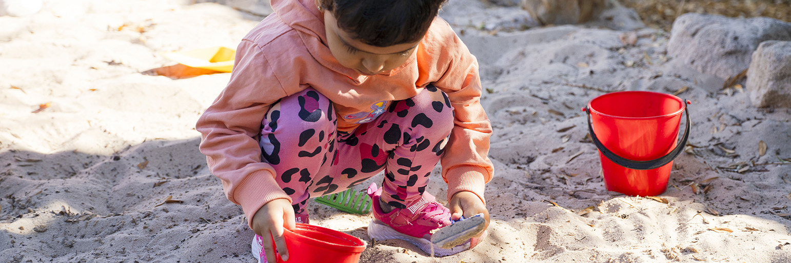 Children playing with plastic toy trucks in a sandpit